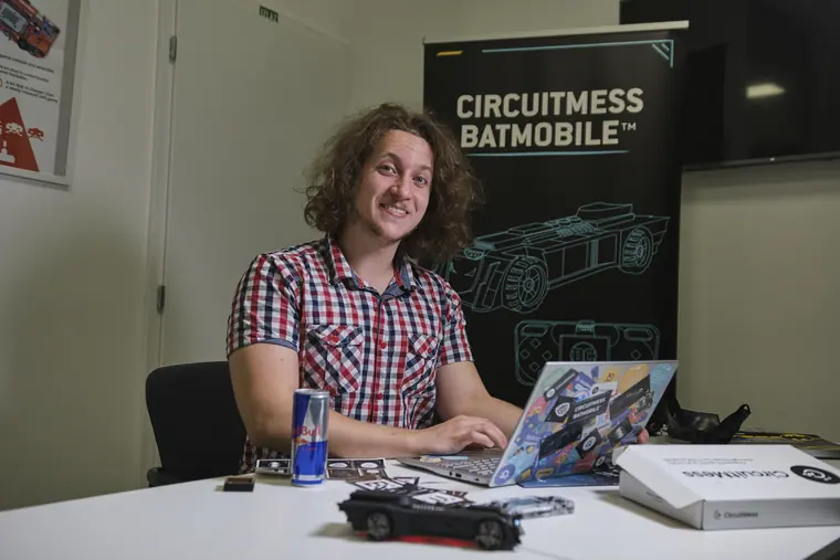 At a desk in front of a CIRCUITMESS BATMOBILE banner, laptop open and the model car parked on the desk