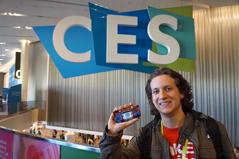 Holding a handheld console up beside the CES lettering on a Las Vegas convention wall