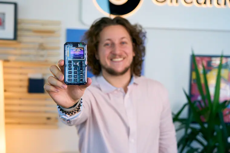 Half-length with MAKERphone 2.0 raised, screen showing the dialler