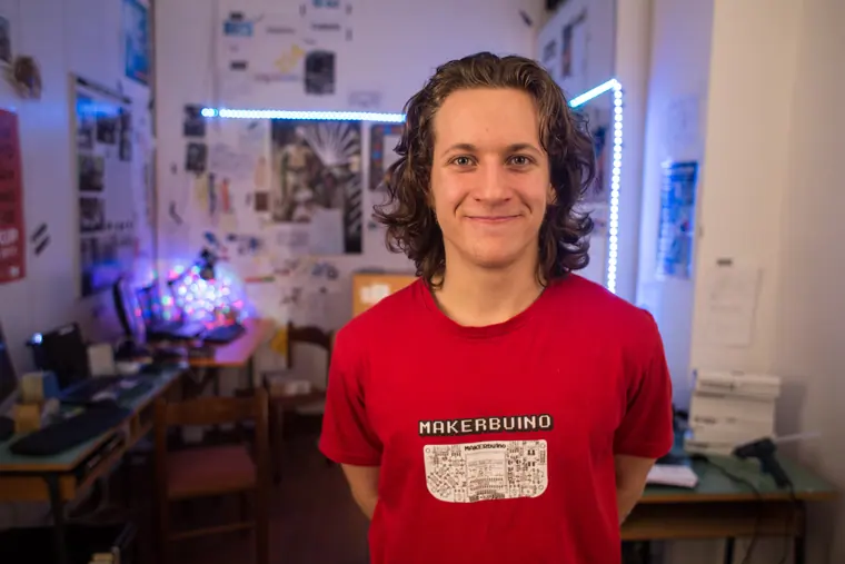 Waist-up portrait in a red MAKERbuino tee, the old workshop soft behind him