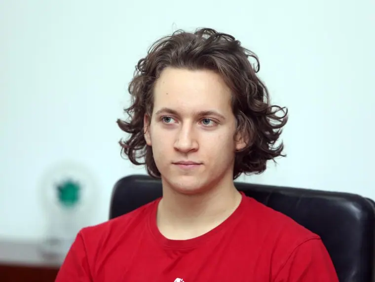 Plain seated portrait in a red tee against an office wall — flat light, no props