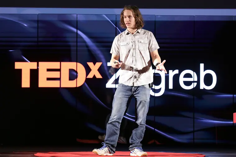 Alone on the TEDxZagreb stage, full body and arms mid-gesture, the wordmark lit across the LED wall behind him